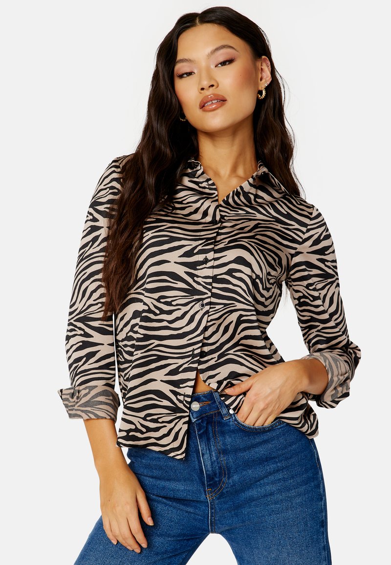 Camicia a maniche lunghe con bottoni in beige con strisce zebrate nere; realizzata in tessuto leggero con colletto e polsini arrotolati.