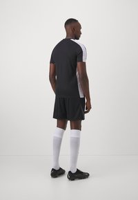 Schwarz-wei�ßes Sporttrikot mit kurzen Ärmeln, kombiniert mit schwarzen Shorts. Verfügt über weiße Akzentuierungen und knielange weiße Socken. Schuhwerk: schwarze Fußballschuhe.