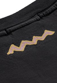 Czarna tkanina prezentująca zygzakowaty wzór w różowym i żółtym kolorze, z textured powierzchnią w okolicach dekoltu odzieży.