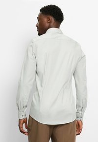 Lichtgrijze lange mouw shirt, gladde stof, aansluitend ontwerp, puntige kraag, enkele knoopmanchetten, subtiele verticale textuur, rugplooien.