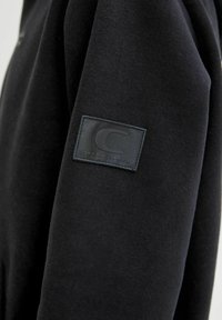 Felpa nera con tessuto testurizzato e una toppa rettangolare con un logo sulla spalla sinistra.