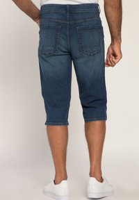 Capris de mezclilla en azul oscuro, con un corte relajado, dobladillos enrollados y bolsillos traseros. Combinados con zapatillas blancas.