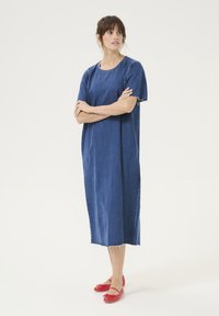Denim midi obleka v temno modri barvi s kratkimi rokavi, sproščenim krojem in strgano robom. Kombinirana z rdečimi balerinkami, ki imajo pentlje.