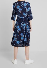 Marinblå klänning med blommigt mönster i blått och burgunder, trekvartsärmar och utsvängd nederkant, kombinerad med vita sneakers.