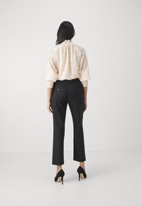 Crèmefärgad topp med hög krage, kombinerad med svarta skräddarsydda byxor och svarta högklackade skor, sedd från baksidan.