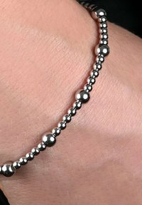 Bracciale di perline argentate su un polso, caratterizzato da una serie di perle sferiche di diverse dimensioni, superficie lucida, texture liscia e design semplice.