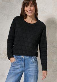 Svart stickad tröja med geometriskt mönster, rund halsringning och långa ärmar, kombinerad med ljusblå denimjeans.