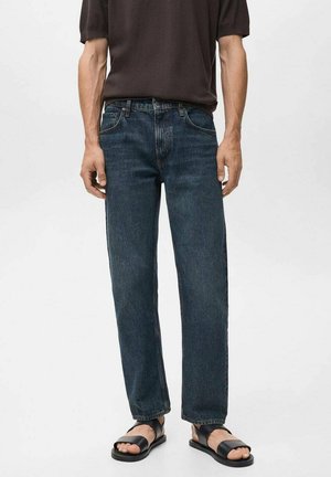 Jeans dritti blu scuro in denim, con un classico design a cinque tasche. Indossati con una camicia corta marrone e sandali neri.