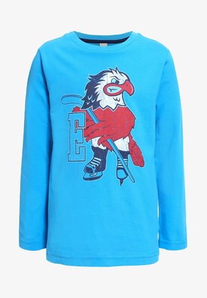 Chemise bleue à manches longues avec un graphisme d’un oiseau rouge et blanc portant des patins à glace et tenant un bâton de hockey à côté d’une grande lettre E.