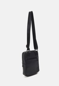 Černá crossbody taška vyrobená z texturované kůže, se zipem hlavní kapsy a přední zipovou kapsou. Nastavitelný popruh s kovovými doplňky.