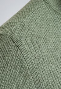 Groene gebreide stof die een textuurpatroon toont met een wafelachtige structuur. Het materiaal heeft duidelijke ribbelaccenten langs de randen.