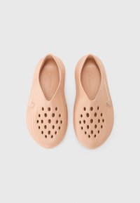 Perzikkleurige instap schoenen met een ronde vorm, geperforeerde bovenkant voor ventilatie, en een klein zilveren Nike-logo aan de zijkant.