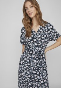 Vestito floreale nero con maniche corte, caratterizzato da una chiusura con bottoni sul davanti, vita con fiocco e fiori viola e blu su uno sfondo scuro.