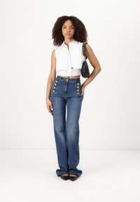 Λευκό αμάνικο πουκάμισο με μπροστινό κουμπί, μπλε ψηλόμεσα τζιν με χρυσά κουμπιά και μαύρη τσάντα.