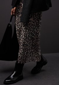 Černé kotníkové boty zkombinované s plisovanou sukni s leopardím potiskem. Textilie má hladký povrch, splývavý design a tmavé tóny.