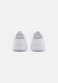 Weiße Sneaker mit einem glatten Lederobermaterial, verstärktem Fersenbereich und einer strukturierten Gummisohle. Lacoste-Logo auf der Ferse geprägt.
