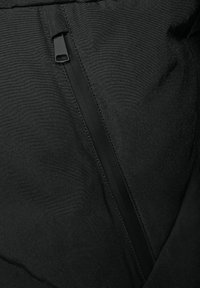 Tessuto nero con una texture liscia dotato di una cerniera nascosta al centro. Dettagli di cucitura lungo la linea della cerniera.