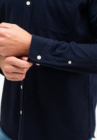 Navyblauwe knoopshirt gemaakt van soepele stof, met een borstzak, witte knopen en verstelbare manchetten.