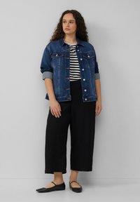 Jeansjack met knoopsluiting, donkerblauwe kleur. Gestreept T-shirt eronder, zwarte wijde broek en platte zwarte schoenen. Gladde texturen.