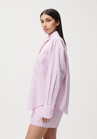 Camicia over-size a righe rosa con chiusura a bottoni, maniche lunghe e tasca sul petto, abbinata a pantaloni corti fitted dello stesso colore. Tessuto dalla superficie liscia.