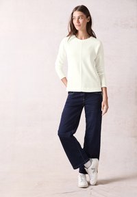 Lichtgroen geribbeld sweater met een ronde halslijn, gecombineerd met donkerblauwe wijde broek en witte sneakers. Eenvoudig, casual outfitontwerp.