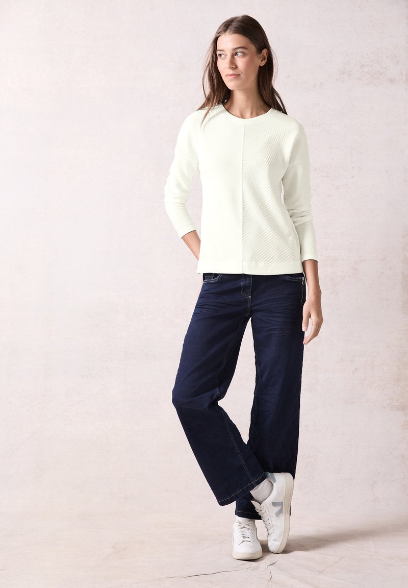 Lichtgroen geribbeld sweater met een ronde halslijn, gecombineerd met donkerblauwe wijde broek en witte sneakers. Eenvoudig, casual outfitontwerp.