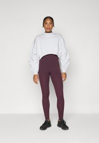 Grå cropped sweatshirt og maroon tights, begge laget av mykt stoff. Svarte joggesko fullfører antrekket. Enkelt design uten mønstre.