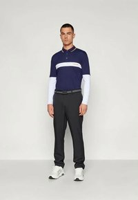 Ναυτικό πόλο μπλουζάκι με λευκή ρίγα στο στήθος και πορτοκαλί λεπτομέρεια, σε συνδυασμό με μαύρο παντελόνι. Λευκά αθλητικά παπούτσια ολοκληρώνουν την εμφάνιση. Απαλή υφασμάτινη υφή.