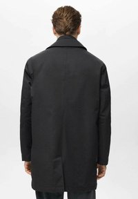Abrigo negro con una textura suave, cuello ancho y mangas largas. La parte posterior presenta un corte recto con una sola costura en el centro.