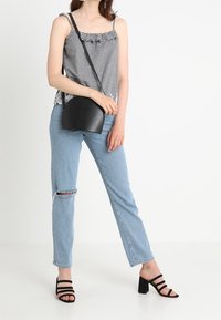 Black and white checkered top with frilled neckline, light blue distressed jeans, and black heeled sandals with vertical straps. Black bag.