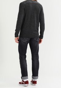 Grauer Strickpulli, dunkle Jeans mit aufgerollten Säumen und roten Turnschuhen. Weicher Stoff, figurbetonter Schnitt und zwei Gesäßtaschen bei den Jeans.