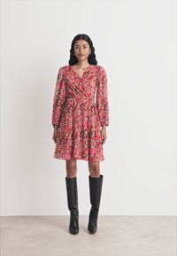 Floral dress in pink and red tones, featuring long sleeves, wrap design, and a flared skirt. Paired with tall black boots.