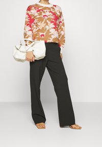 Pull en tricot crème avec un motif floral marron et rose ; pantalon noir à jambes larges ; sac doux blanc ; sandales à talons tan.