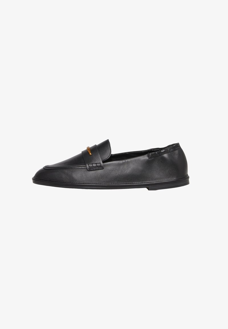 Mocassin en cuir noir avec semelle plate basse et petit accent doré sur la bride, conçu pour un confort sans enfiler.