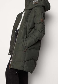 Olivově zelená prošívaná bunda s kapucí, se zipovým zapínáním, bočními kapsami a hnědými dekorativními detaily. Texturovaná látka s prošívaným vzorem.