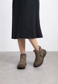 Botas de tobillo marrones con un suave borde de piel de pelo, cierre de cremallera y parte superior de ante texturizado. Punta redondeada y suela gruesa para mayor comodidad y estabilidad.