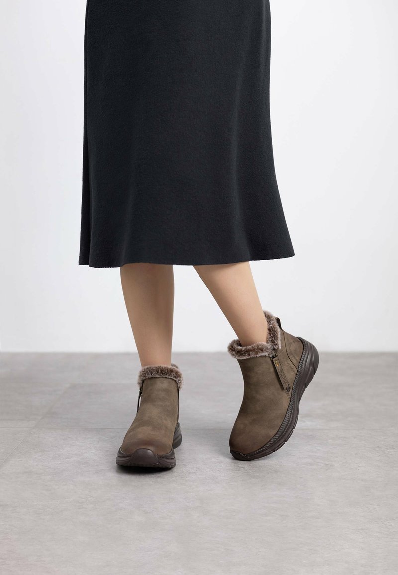 Botas de tobillo marrones con un suave borde de piel de pelo, cierre de cremallera y parte superior de ante texturizado. Punta redondeada y suela gruesa para mayor comodidad y estabilidad.