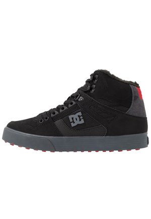 Baskets montantes noires avec semelle grise et détail rouge au talon, avec lacets, col matelassé et logo DC sur le côté.
