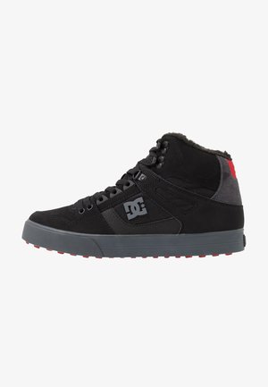 Zwarte hoge sneaker met grijze zool en rode hieldetail, voorzien van veters, gevoerde kraag en DC merklogo aan de zijkant.