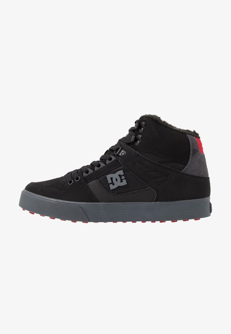 Baskets montantes noires avec semelle grise et détail rouge au talon, avec lacets, col matelassé et logo DC sur le côté.