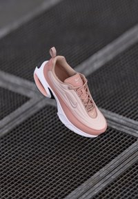 Chaussure Nike Air Max en rose clair avec une tige texturée, des contours lisses, une semelle blanche et des accents noirs contrastants au niveau du talon et sur le côté.