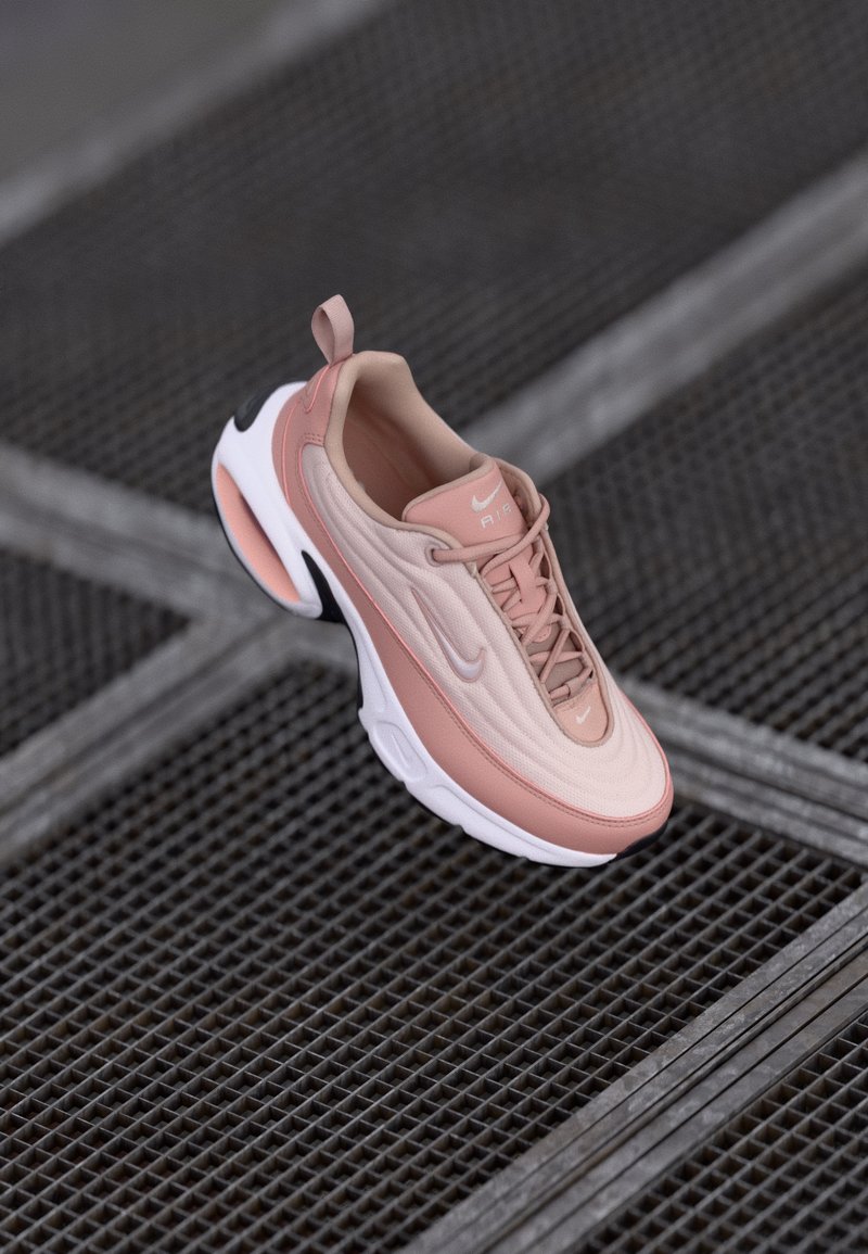 Chaussure Nike Air Max en rose clair avec une tige texturée, des contours lisses, une semelle blanche et des accents noirs contrastants au niveau du talon et sur le côté.