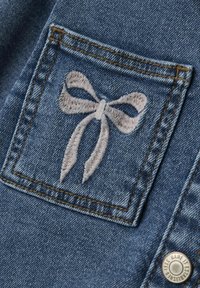 Denimtyg i ljusblå färg har ett dekorativt broderad rosett i ljusrosa på bakfickan. Guldtråd framhäver kanterna.