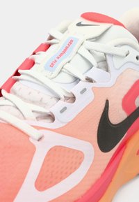 Αθλητικό παπούτσι Nike με επάνω μέρος από δίχτυ σε αποχρώσεις του ροζ και λευκού, μαύρο λογότυπο swoosh, κόκκινες αντιθετικές λεπτομέρειες και υφή στη σόλα.