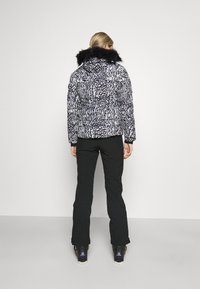 Doudoune imprimé animal noir et blanc, avec une capuche en fausse fourrure, portée avec un pantalon noir et des bottes de ski, vue de dos.