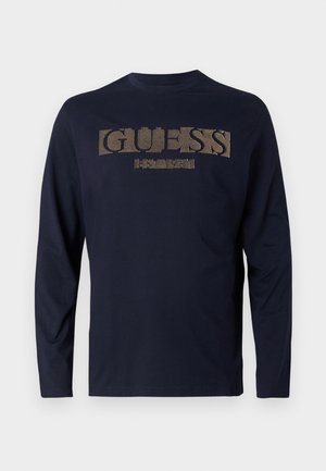 Marineblauwe T-shirt met lange mouwen van katoen, met een textuur in goud van het "GUESS" logo over de borst en een ronde halslijn.