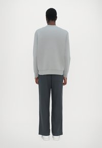 Gray sweatshirt with long sleeves and ribbed hem, paired with dark gray wide-leg pants. Model facing away shows a relaxed fit. White sneakers.