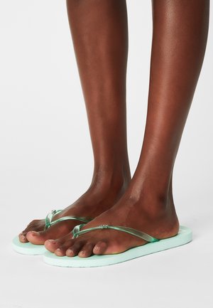 Mintgrønne flip-flops med gennemsigtige remme og en tekstureret fodseng. Sålen er flad og let tykkere, hvilket giver et minimalistisk design.
