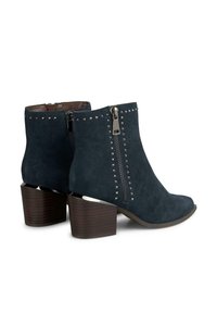 Botas de ante hasta el tobillo en azul marino con una cremallera lateral, decoradas con tachuelas plateadas en la parte frontal. Los tacones en acabado de madera oscura completan el diseño.