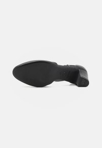 Scarpa nera con tacco, in pelle liscia, con punta arrotondata e suola in gomma testurizzata. Presenta un logo discreto vicino al tallone.
